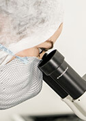 Mujer con cofia y cubrebocas blanco viendo a través de microscopio, mientras realiza análisis fisicoquímico de materia prima producida por Tecnoalimentos para la producción de alimento para ganadería en Querétaro